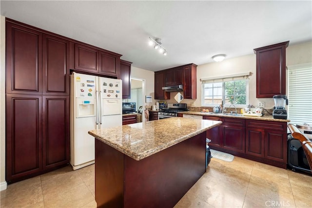 kitchen with sink, white refrigerator with ice dispenser, a center island, gas range, and light stone countertops