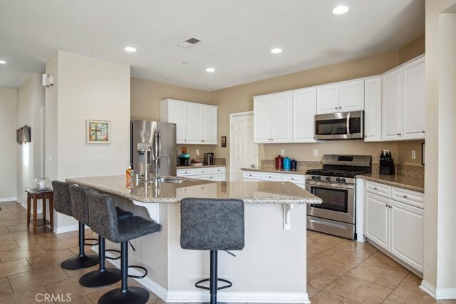 kitchen with a kitchen island with sink, white cabinetry, stainless steel appliances, and a kitchen breakfast bar