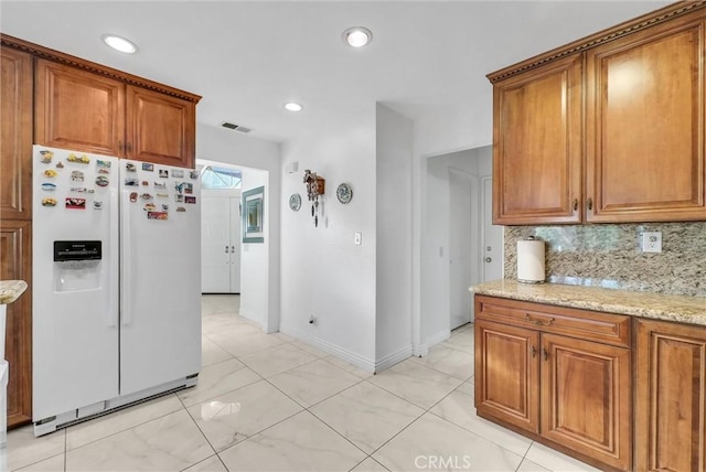 kitchen featuring light stone counters, decorative backsplash, and white fridge with ice dispenser