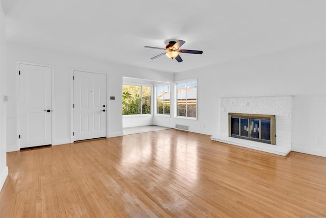 unfurnished living room with ceiling fan, a brick fireplace, and light hardwood / wood-style floors