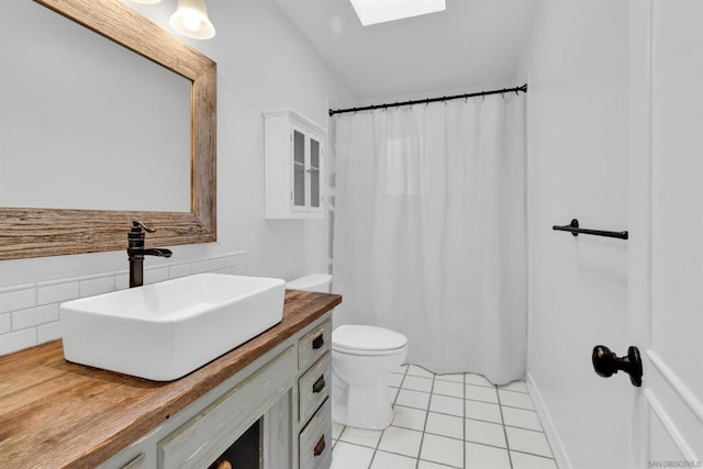 bathroom with curtained shower, a skylight, tile patterned flooring, vanity, and toilet