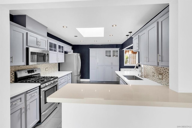 kitchen featuring sink, a skylight, stainless steel appliances, decorative light fixtures, and kitchen peninsula