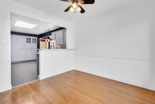 interior space with gray cabinets, ceiling fan, a skylight, kitchen peninsula, and light wood-type flooring