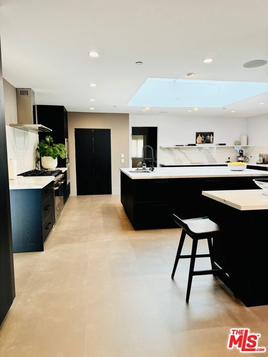 kitchen with sink, a breakfast bar area, backsplash, stainless steel range with gas stovetop, and wall chimney range hood