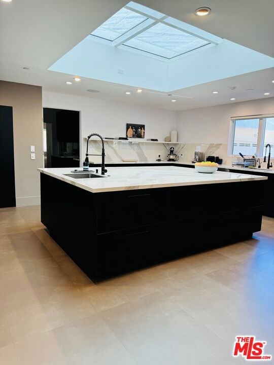 kitchen with a large island, a skylight, sink, and backsplash