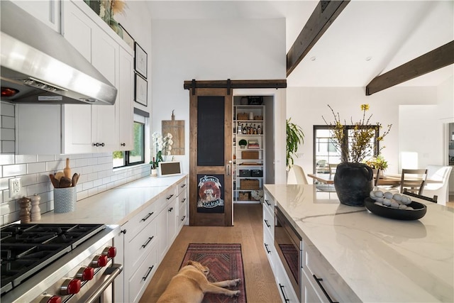 kitchen with high end stainless steel range oven, white cabinetry, a barn door, and light stone counters