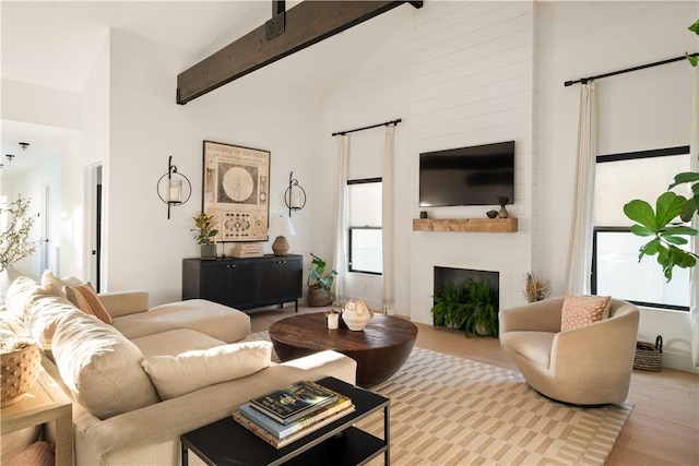 living room featuring a fireplace, beam ceiling, high vaulted ceiling, and light wood-type flooring