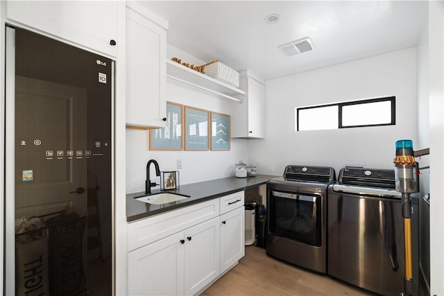 clothes washing area with separate washer and dryer, sink, light hardwood / wood-style floors, and cabinets