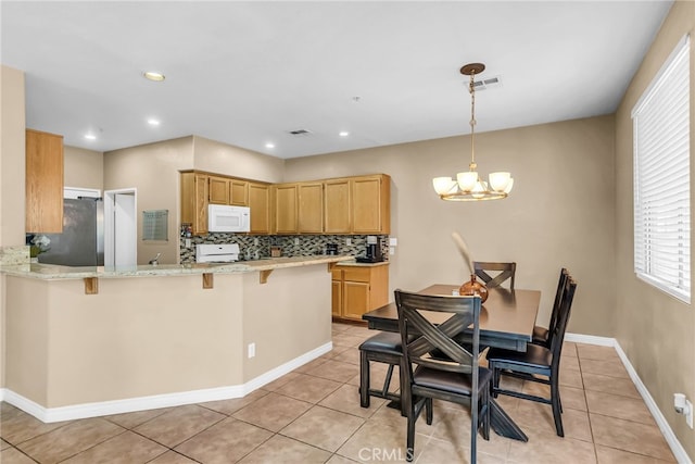 kitchen featuring tasteful backsplash, stainless steel fridge, a chandelier, a kitchen bar, and kitchen peninsula