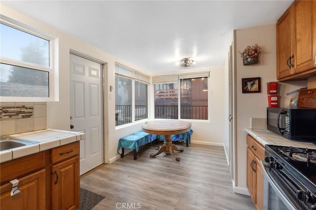 kitchen with stainless steel range with gas stovetop, tile countertops, backsplash, and light hardwood / wood-style flooring