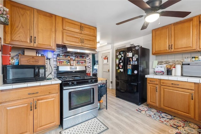 kitchen with tasteful backsplash, tile countertops, light hardwood / wood-style floors, and black appliances