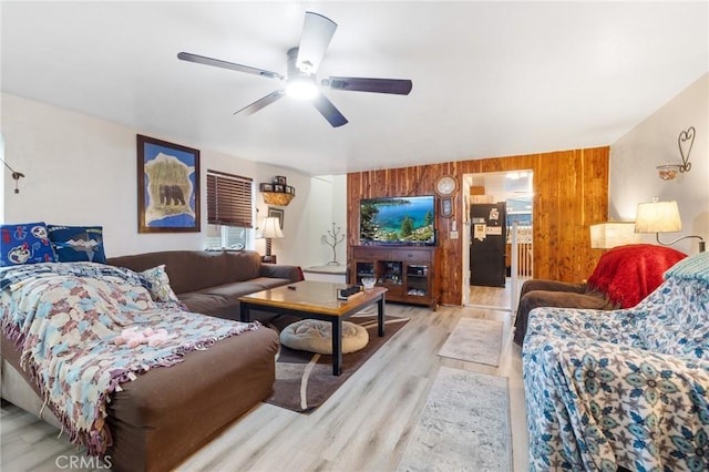 living room with ceiling fan, light wood-type flooring, and wooden walls