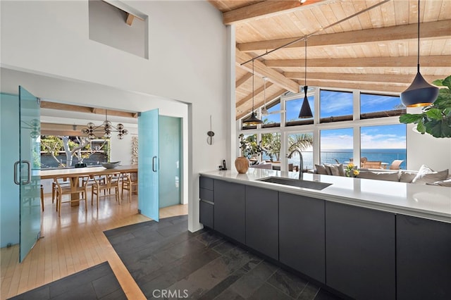 kitchen with beamed ceiling, a water view, sink, and decorative light fixtures