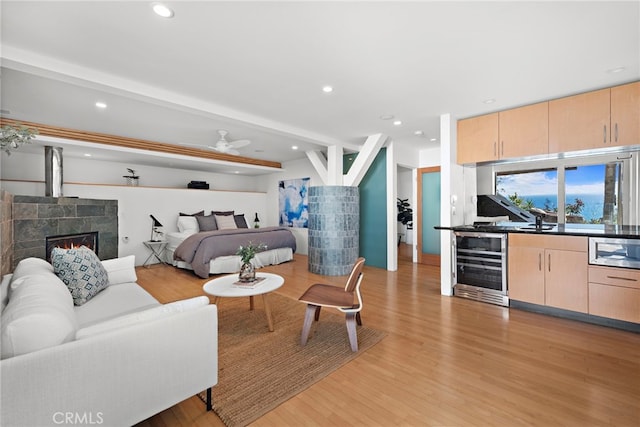 bedroom with wine cooler, a fireplace, beam ceiling, and light wood-type flooring