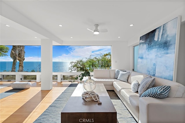 living room with ceiling fan, a water view, and light hardwood / wood-style floors