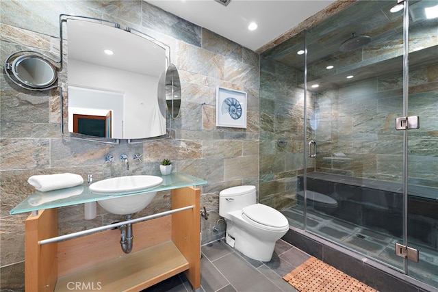 bathroom featuring a shower with door, sink, tile walls, and toilet