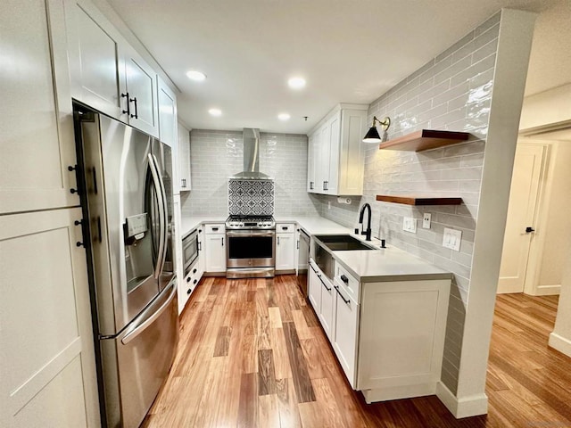 kitchen featuring stainless steel appliances, white cabinetry, light wood-type flooring, and wall chimney exhaust hood