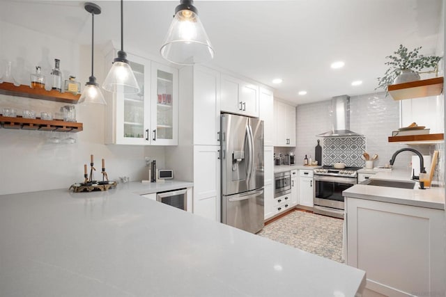 kitchen featuring stainless steel appliances, white cabinetry, decorative light fixtures, and wall chimney exhaust hood