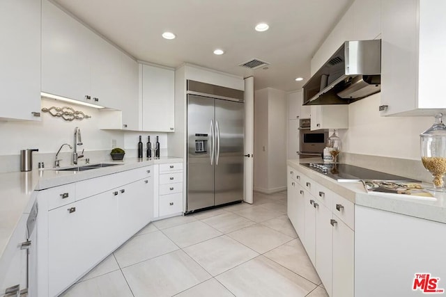 kitchen with sink, white cabinetry, light tile patterned floors, appliances with stainless steel finishes, and wall chimney range hood