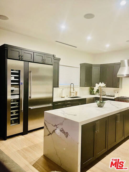 kitchen featuring premium range hood, sink, a center island, high quality fridge, and light stone countertops