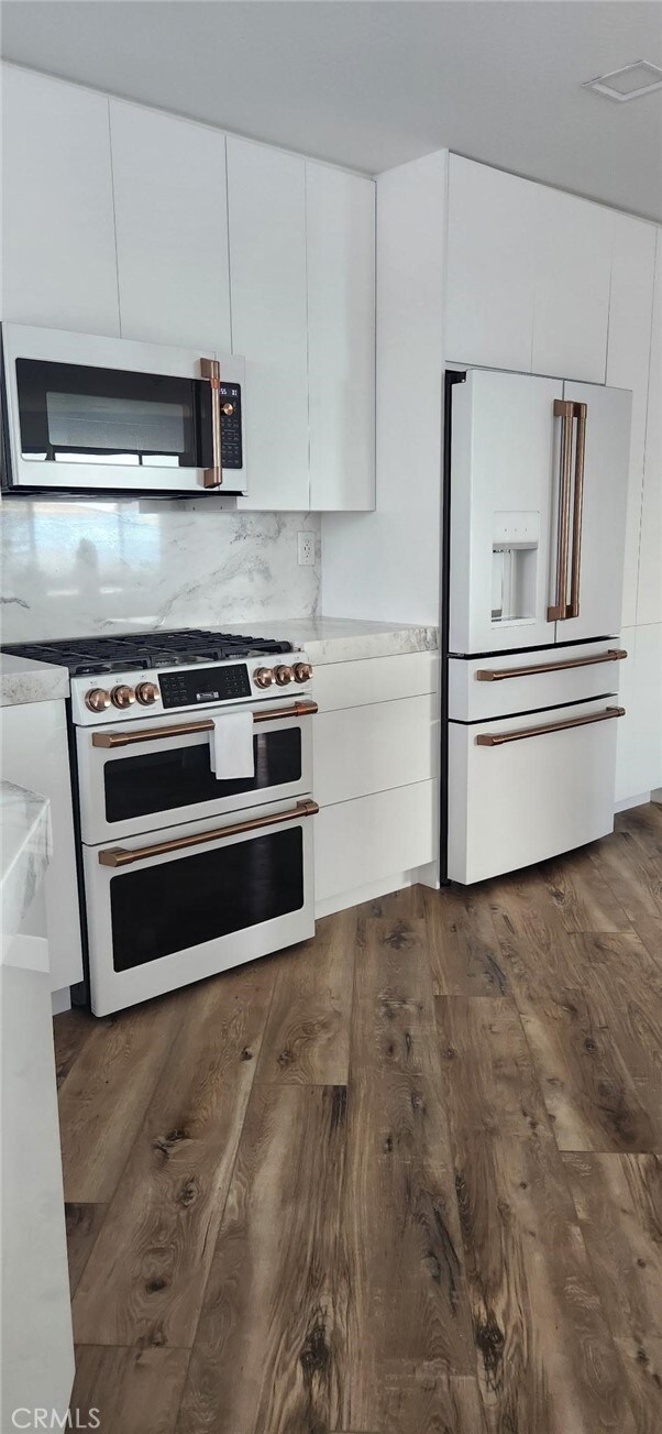 kitchen featuring dark hardwood / wood-style flooring, premium appliances, backsplash, and white cabinets