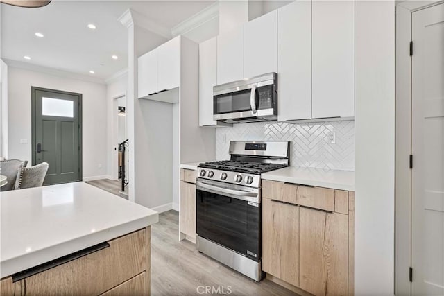 kitchen with white cabinetry, crown molding, appliances with stainless steel finishes, light hardwood / wood-style floors, and backsplash