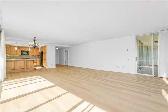 unfurnished living room with an inviting chandelier and light hardwood / wood-style floors