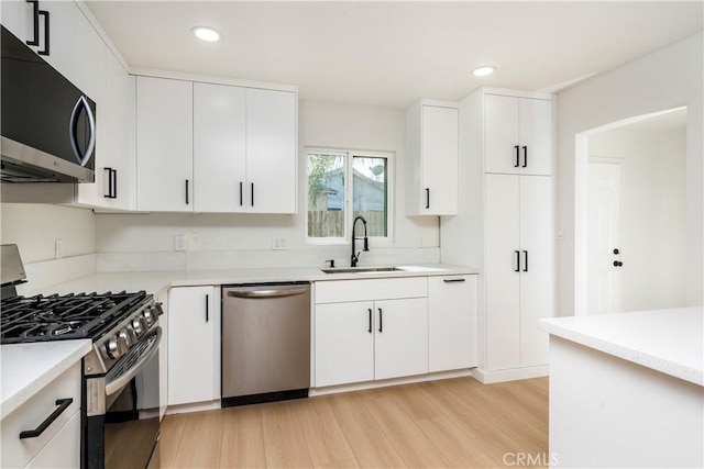 kitchen with stainless steel appliances, sink, light hardwood / wood-style flooring, and white cabinets