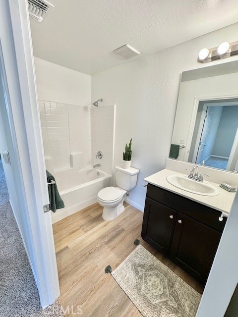 full bathroom with washtub / shower combination, hardwood / wood-style floors, vanity, a textured ceiling, and toilet