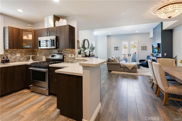 kitchen featuring light countertops, appliances with stainless steel finishes, open floor plan, dark brown cabinets, and a peninsula