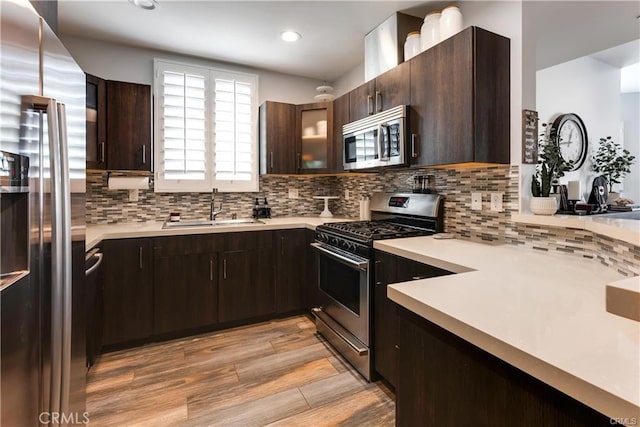 kitchen with light countertops, decorative backsplash, appliances with stainless steel finishes, a sink, and light wood-type flooring