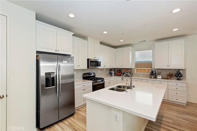 kitchen featuring sink, stainless steel appliances, an island with sink, white cabinets, and light wood-type flooring