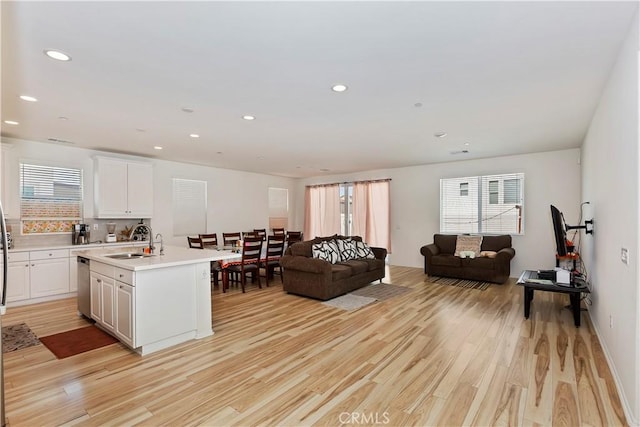 kitchen with dishwasher, sink, white cabinets, a kitchen island with sink, and light hardwood / wood-style floors