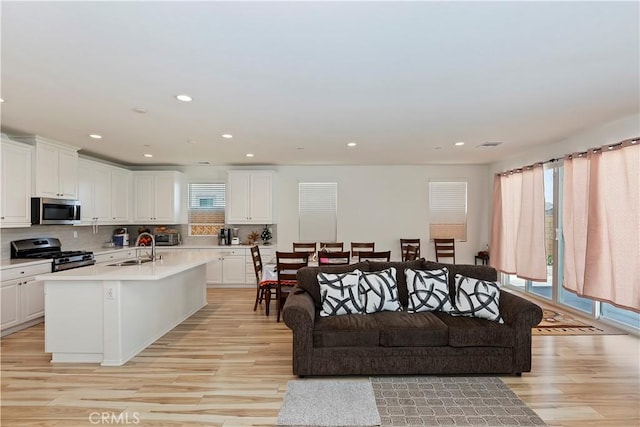 kitchen with white cabinetry, tasteful backsplash, appliances with stainless steel finishes, a kitchen island with sink, and light hardwood / wood-style floors