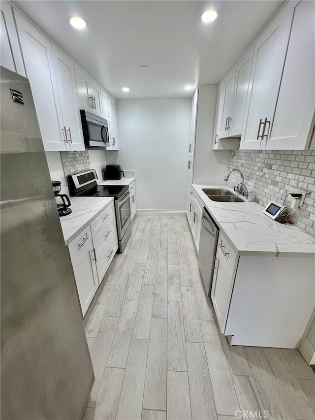 kitchen featuring appliances with stainless steel finishes, light wood-style floors, white cabinets, a sink, and light stone countertops