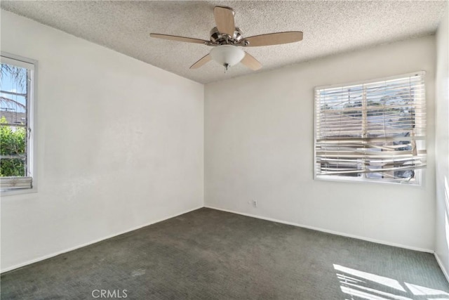 empty room featuring dark colored carpet, ceiling fan, and a textured ceiling