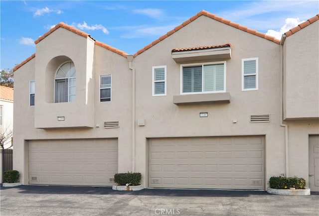 view of front facade with a garage, a tiled roof, and stucco siding