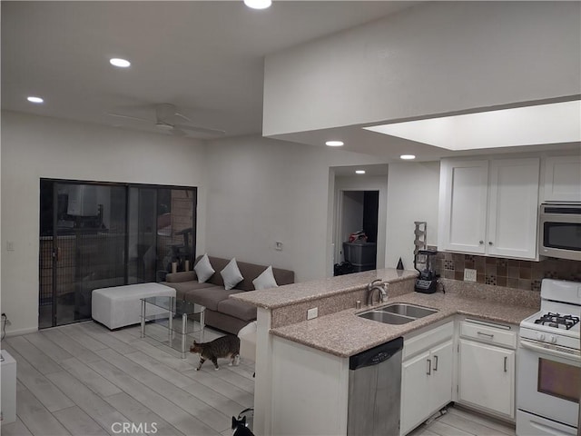 kitchen featuring a peninsula, a sink, white cabinetry, light countertops, and appliances with stainless steel finishes