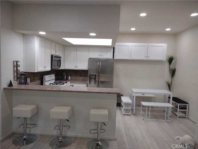 kitchen with a breakfast bar area, white cabinetry, backsplash, stainless steel appliances, and kitchen peninsula