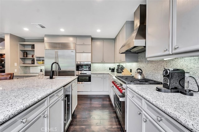 kitchen with wine cooler, wall chimney exhaust hood, premium appliances, dark hardwood / wood-style flooring, and light stone countertops