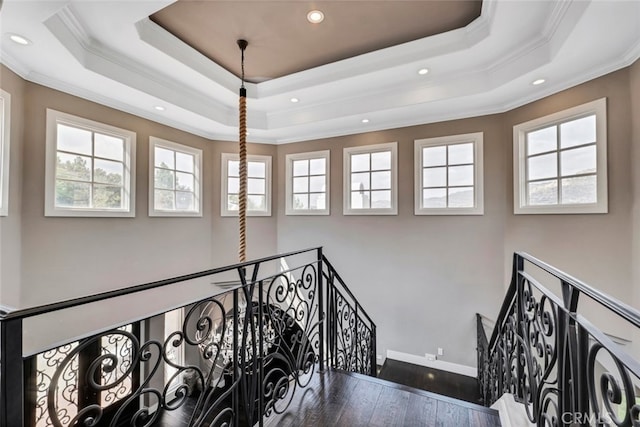 stairs with ornamental molding, a healthy amount of sunlight, and a raised ceiling