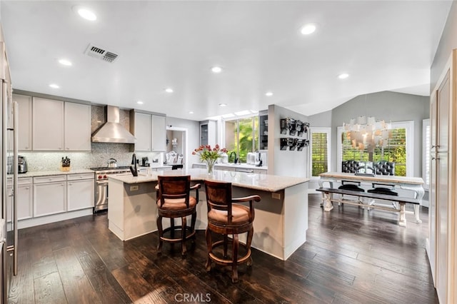 kitchen with high end stove, a center island with sink, light stone counters, and wall chimney exhaust hood