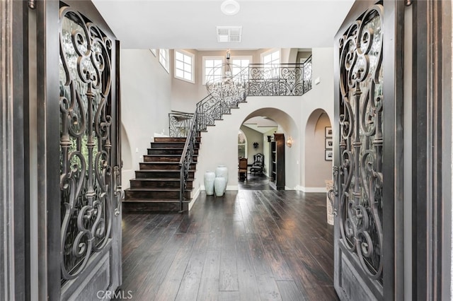 foyer entrance featuring a towering ceiling, dark hardwood / wood-style flooring, and a notable chandelier