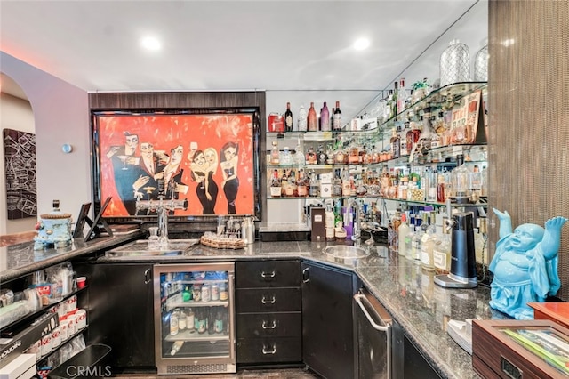 bar featuring sink, dark stone countertops, and beverage cooler