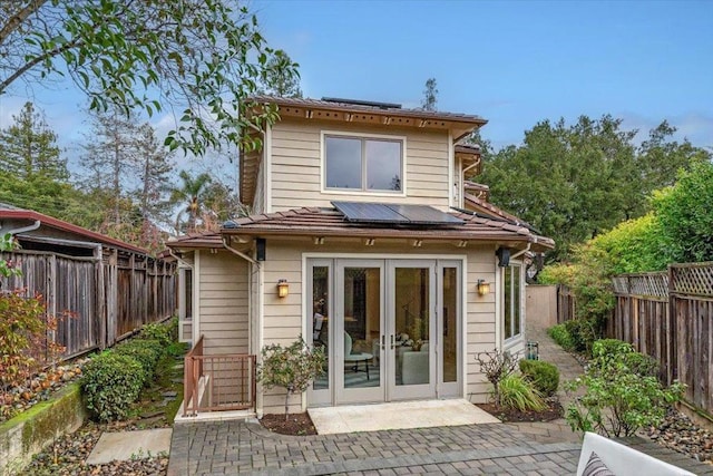 back of property with french doors, a patio area, and solar panels