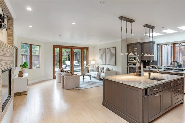 kitchen featuring pendant lighting, light stone countertops, sink, and dark brown cabinets