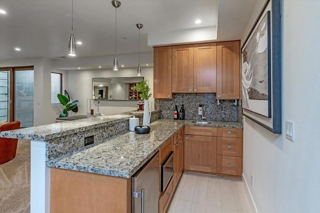 kitchen with pendant lighting, kitchen peninsula, light stone counters, and backsplash