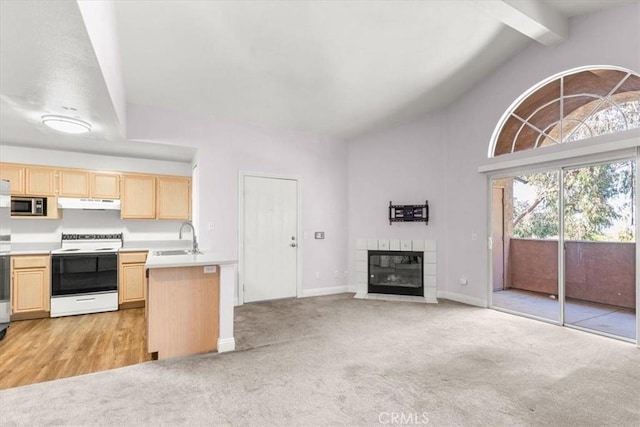 kitchen featuring sink, white electric range oven, a tiled fireplace, light colored carpet, and light brown cabinets