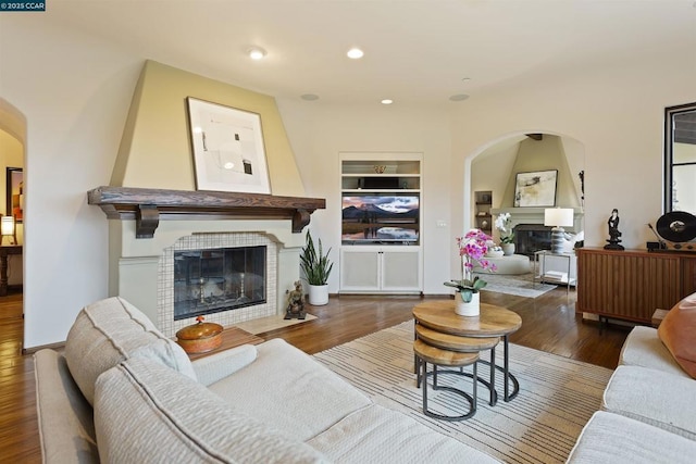 living room with a tiled fireplace, dark wood-type flooring, and built in shelves