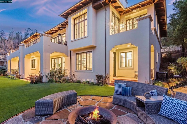 back house at dusk featuring a yard, a balcony, and an outdoor fire pit